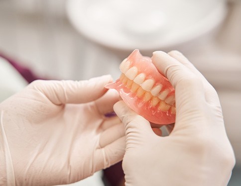 White-gloved hands holding a full set of dentures