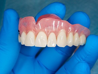 Closeup of an upper set of dentures held by blue-gloved hand