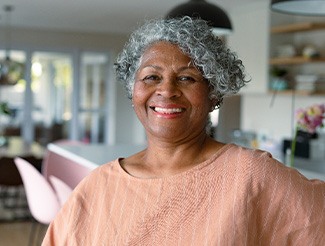 Senior woman in peach-colored shirt smiling in kitchen