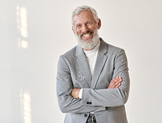 Senior man in grey shirt smiling with arms folded