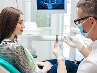 Dentist wearing white showing model implant to patient with long brown hair