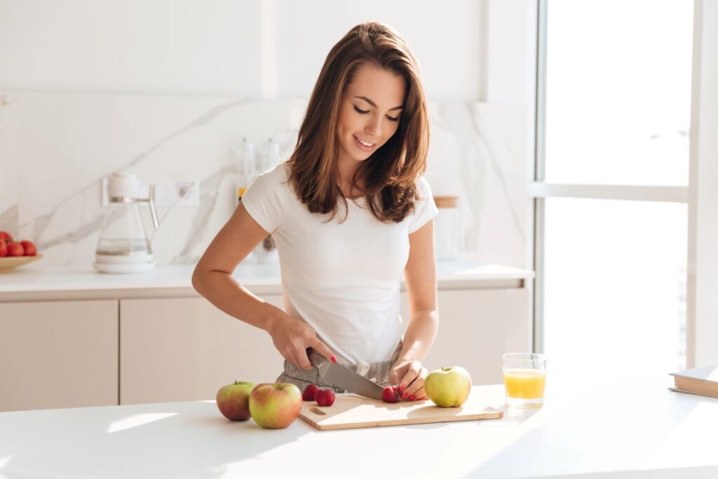 A woman in the kitchen cutting an apple.